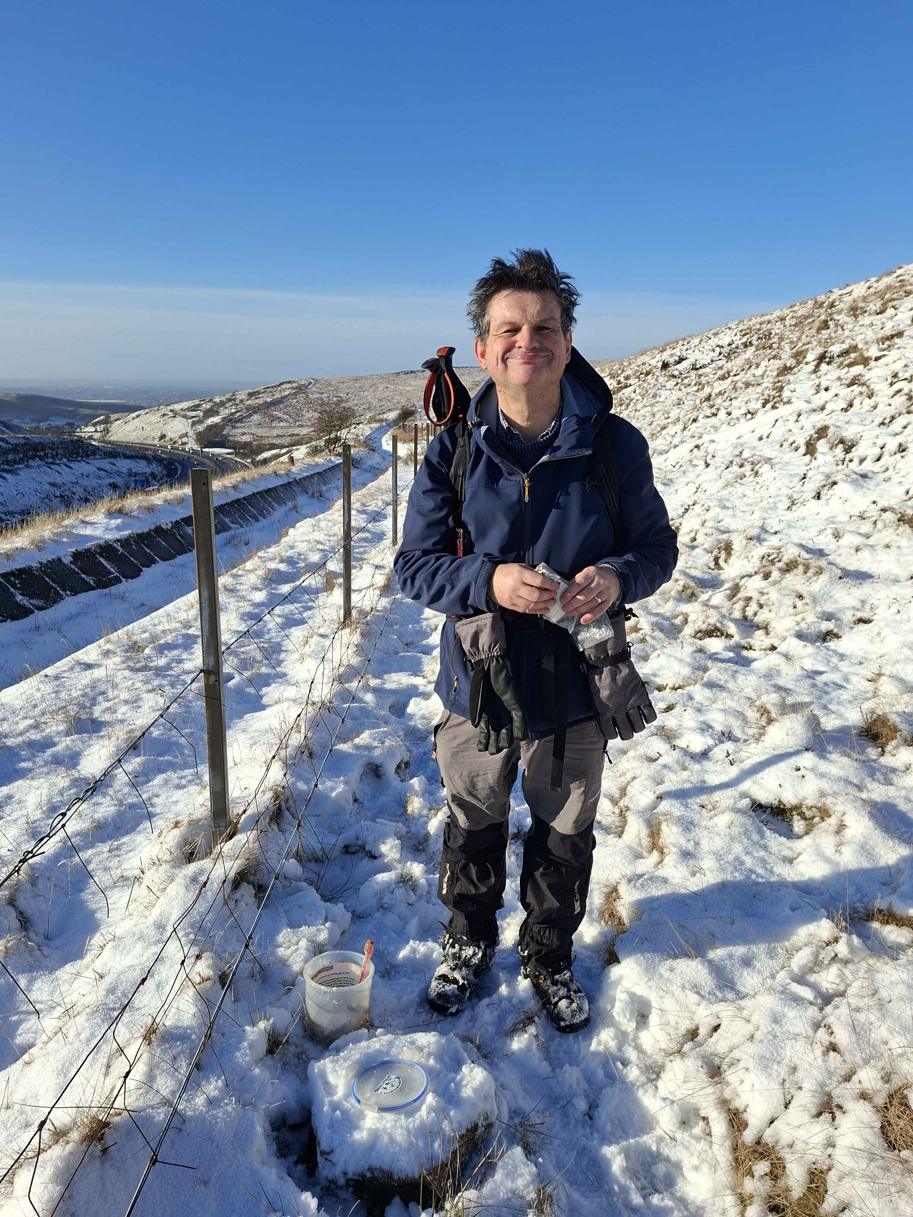 Simon standing on snowy hillside with open geocache container by feet